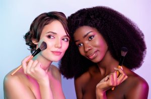 White girl and black girl facing each other and using blusher brushes